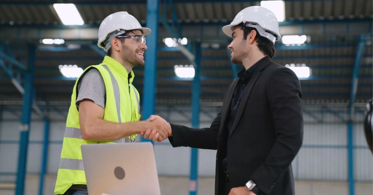 Engineer and manager shaking hands in manufacturing facility.